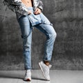 Sport woman legs in blue jeans in silver thin down puffer jacket white sneakers Royalty Free Stock Photo