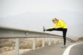 Sport woman stretching leg muscle after running workout on asphalt road with dry desert landscape in hard fitness training session Royalty Free Stock Photo