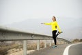 Sport woman stretching leg muscle after running workout on asphalt road with dry desert landscape in hard fitness training session Royalty Free Stock Photo