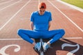 Sportive Caucasian athlete doing stretching exercises sitting on the running track. Runner male sitting on running track with feet