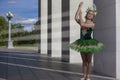 Sportive Caucasian Ballet Dancer in Green Tutu Dress Standing With Hands Lifted in Stretching Dance Pose Near Pillar Wall