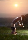 Attractive slim young woman doing yoga exercises outdoors on background of beautiful sky.