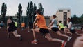 Sportive people group doing exercises strething, squating at stadium