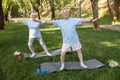 Sportive tranquil senior man and woman do yoga exercise on lawn