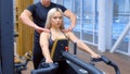 Sportive woman is doing exercises for spine muscles on block rowing simulator.