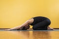 Sportive woman practicing yoga performs a balasana exercise, a childs pose, an athlete trains on a mat near a yellow wall