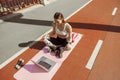 Sportive woman watches video tutorial via laptop sitting on footbridge