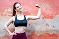 Sportive young girl shows muscules and smile - red wall outdoor copy space