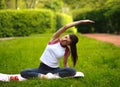 Sportive young woman stretching, doing fitness exercises in park