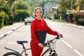 Sports and activity. Portrait of a smiling young beautiful woman in red sportswear standing next to a Bicycle. Side view. In the Royalty Free Stock Photo