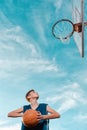 Sports and basketball. A young teen in a black tracksuit playing basketball on the school Playground. Cloudy blue sky with basket Royalty Free Stock Photo