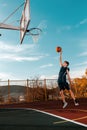 Sports and basketball. A young teenager in a blue tracksuit throws a jump ball into the basket. Blue sky. Vertical Royalty Free Stock Photo