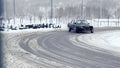 Sports cars drive through a turn on a snow-covered slippery highway.