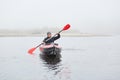 Sports cheerful man in kayak, padding in foggy river in morning, feels happy, laughing sincerely, spending his free time outdoors Royalty Free Stock Photo