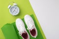 Sports concept. Top view photo of white sneakers over green exercise mat and alarm clock on bicolor green and white background Royalty Free Stock Photo