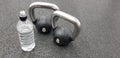 Sports equipment. 2 black kettlebells and a water bottle on the dark rubber floor