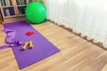 Sports equipment on floor in living room, violet yoga mat, yellow dumbbells, red rubber resistance band and green rubber fitness Royalty Free Stock Photo