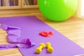 Sports equipment on floor in living room, violet yoga mat, yellow dumbbells, red rubber resistance band and green rubber fitness Royalty Free Stock Photo