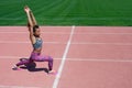 Sports exercises and stretching in the stadium. A young dark-skinned girl in a gray T-shirt, pink pants and sneakers raised her ha Royalty Free Stock Photo