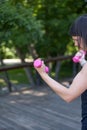 Sports girl holds small womens pink dumbbells. Young woman does outdoor fitness. Copy space. Vertical frame Royalty Free Stock Photo