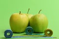 Apples near measuring tape rolls on green background