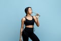 Sports hydration concept. Sporty african american woman drinking mineral water from bottle at blue studio background Royalty Free Stock Photo