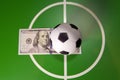 Sports and money concept - Toy soccer ball in a midfield, in the center of the green field and the banknote in hundred dollars on Royalty Free Stock Photo