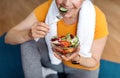 Sports and nutrition concept. Fit senior woman sitting on yoga mat, eating fresh vegetable salad after domestic workout Royalty Free Stock Photo