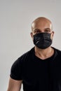 Sports during quarantine. Vertical shot of a strong athletic bald man wearing black medical mask looking at camera while