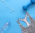 Sports top, blue dumbbell, headphones, water bottle on blue back