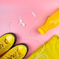 Sports youth style. Yellow sneakers and a bottle of water. Smartphone with headphones on a pink background.