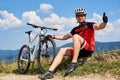 Sportsman bicyclist in sportswear and helmet sitting near his mountain bike on grassy roadside Royalty Free Stock Photo