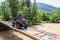 Sportsman in helmet drives ATV crossing river by wooden bridge in Caucasus mountains. Quad bike travel adventure and nature