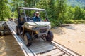 Sportsman in helmet drives SSV crossing river by wooden bridge in Caucasus mountains. Quad bike and buggy travel adventure and