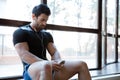 Sportsman listenin to music, using his cellphone sitting on windowcill