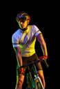 Portrait of young male cyclist on bicycle in cycling shorts and protective helmet isolated on dark background in neon Royalty Free Stock Photo