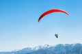 Sportsman on red paraglider soaring over the snowy mountain peak