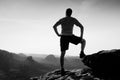 Sportsman in shirt and pants. Man is standing on the peak of sandstone cliff in rock empires park and watching into misty valley.