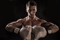 Sportsman with stern look on black background. Man with muscular body wearing boxing gloves. Athlete at