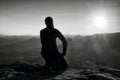 Sportsmann hiker in black sportswear sit on mountain top and take a rest. Tourist watch down to morning misty valley. Royalty Free Stock Photo