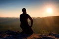 Sportsmann hiker in black sportswear sit on mountain top and take a rest. Tourist watch down to morning misty valley. Royalty Free Stock Photo