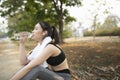 Sportswoman runner wearing earphones drinking water from plastic bottle after workout .