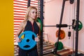 A sportswoman, stands in the gym holding a blue pancake for the bar.
