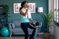 Sporty african young woman exercising on smart stationary bike while drinking water at home Royalty Free Stock Photo