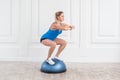 Sporty attractive woman doing exercise in bosu balance trainer, squats on fitness ball. Royalty Free Stock Photo