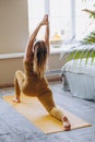 Sporty blonde woman does yoga pose on mat against window