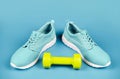 sporty blue sneakers pair with dumbbell on blue background, sport accessory