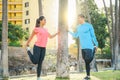 Sporty couple stretching legs leaning on a tree in park at sunset - Two persons training and making legs exercises outdoor Royalty Free Stock Photo