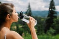 Sporty female drinking water from bottle on background of sunny mountain hills. Outdoor workout Royalty Free Stock Photo