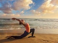 Sporty fit woman practices yoga Anjaneyasana at beach on sunset